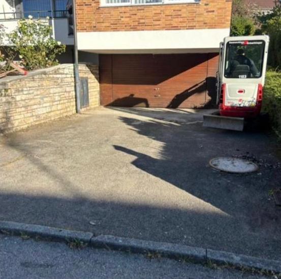 Einfahrt vor dem Umbau: Asphalt und Minibagger vor der Garage